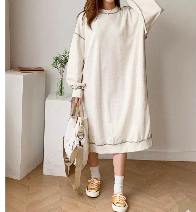Full-body shot of model wearing an oversized oatmeal sweater dress styled casually with yellow shoes and a tote bag.